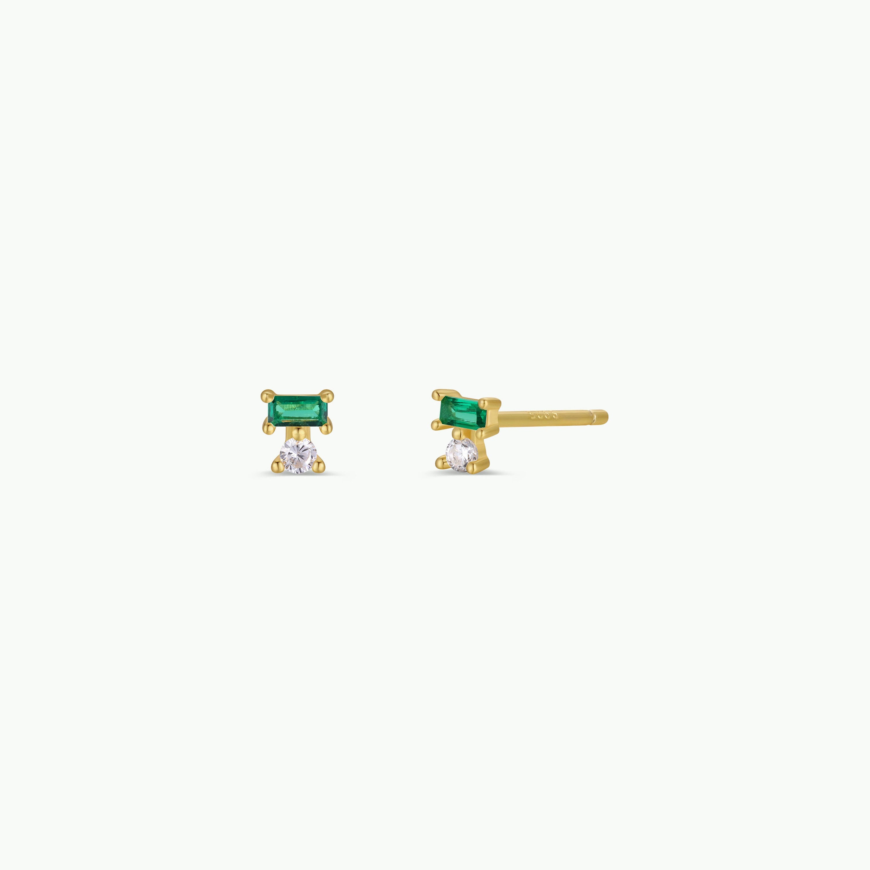 The Emerald Double Stud Stack features small gold stud earrings with an emerald baguette set above a round CZ stone, crafted in 18k gold plating and shown on a plain white background.