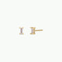 The Clear Baguette features two small baguette stud earrings with clear gemstones in yellow gold prongs and 18k gold plating, displayed front and side on a plain white background.