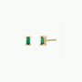 The Emerald Baguette features two gold-plated stud earrings, each showcasing a vertically set rectangular emerald-green gemstone with four prongs, displayed on a plain white background.