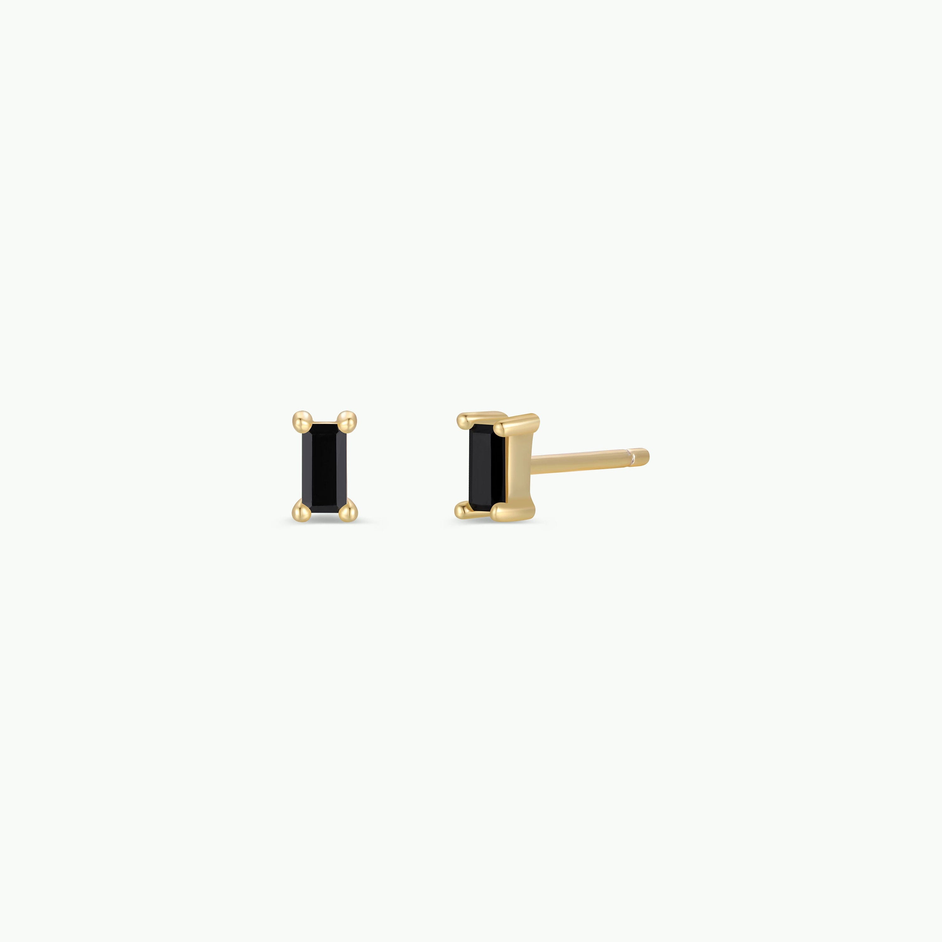 The Black Baguette features a pair of baguette stud earrings with small rectangular black stones set in four prongs, finished with 18k gold plating and sterling silver posts, displayed from the front and side on a white background.