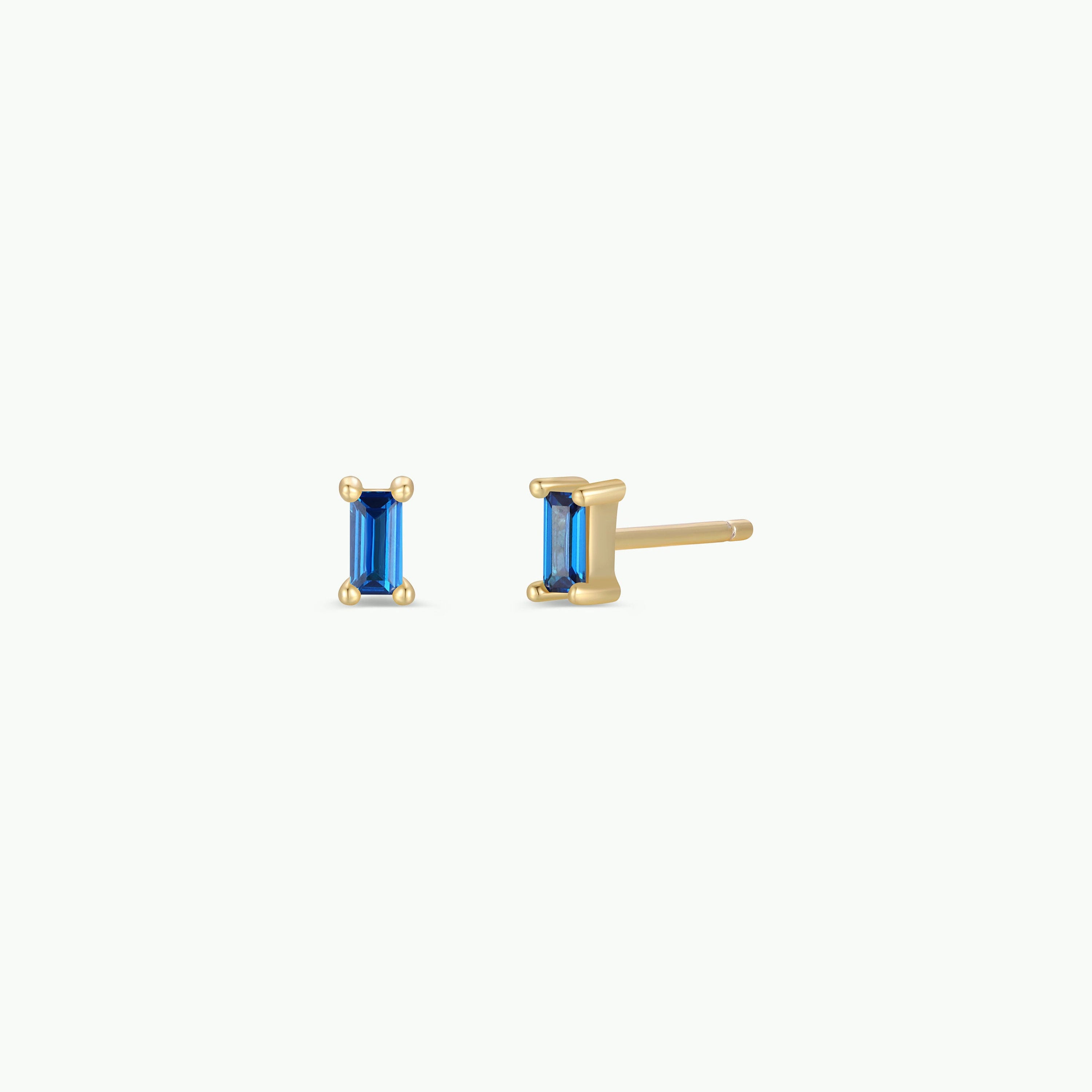 The Sapphire Baguette earrings are gold-plated stud earrings with rectangular blue gemstones, displayed from the front and side on a plain white background.