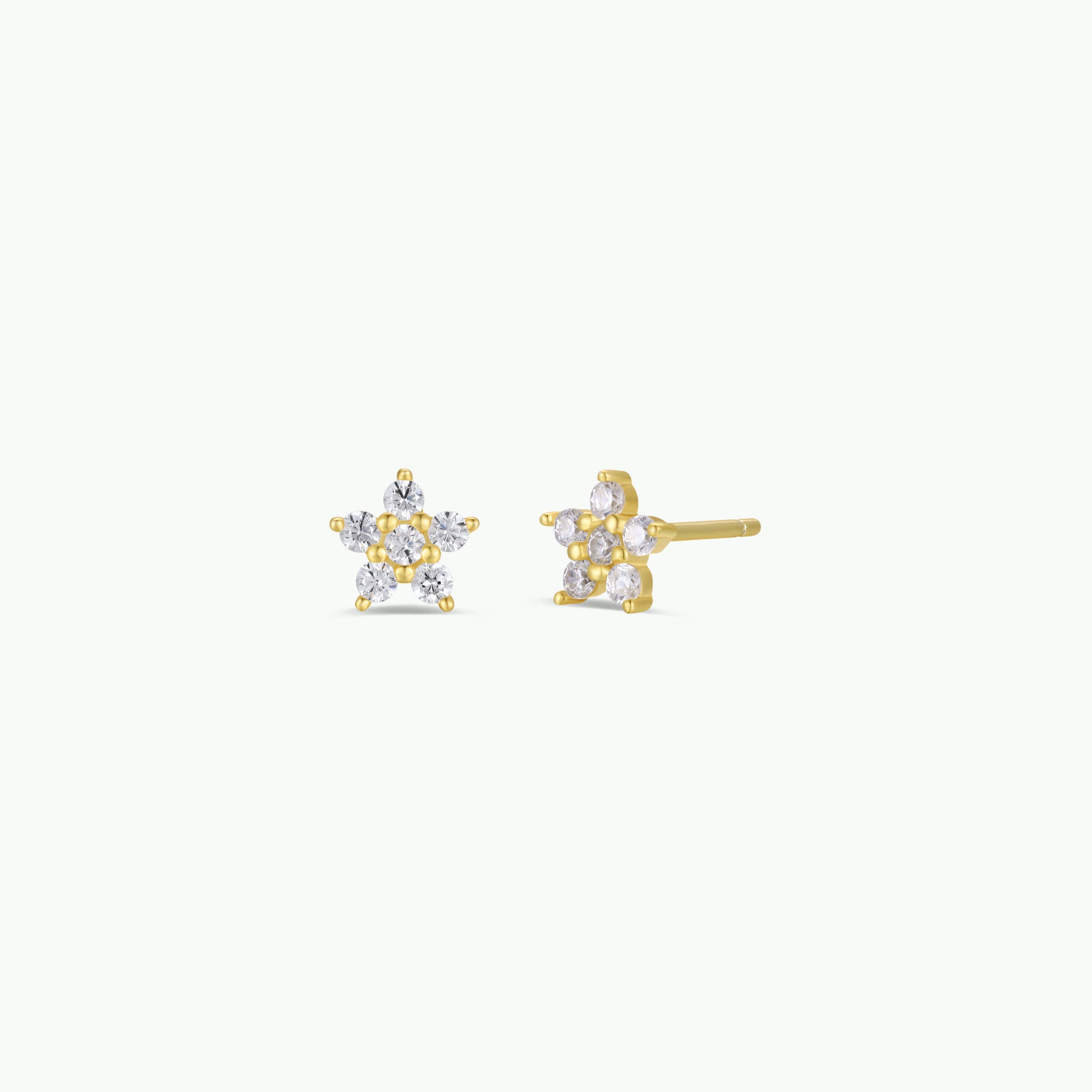 The Pavé Flower earrings are 18k gold plated star studs featuring small, round, clear gemstones on each point and sterling silver posts. These sparkling earrings stand out against a plain white background.
