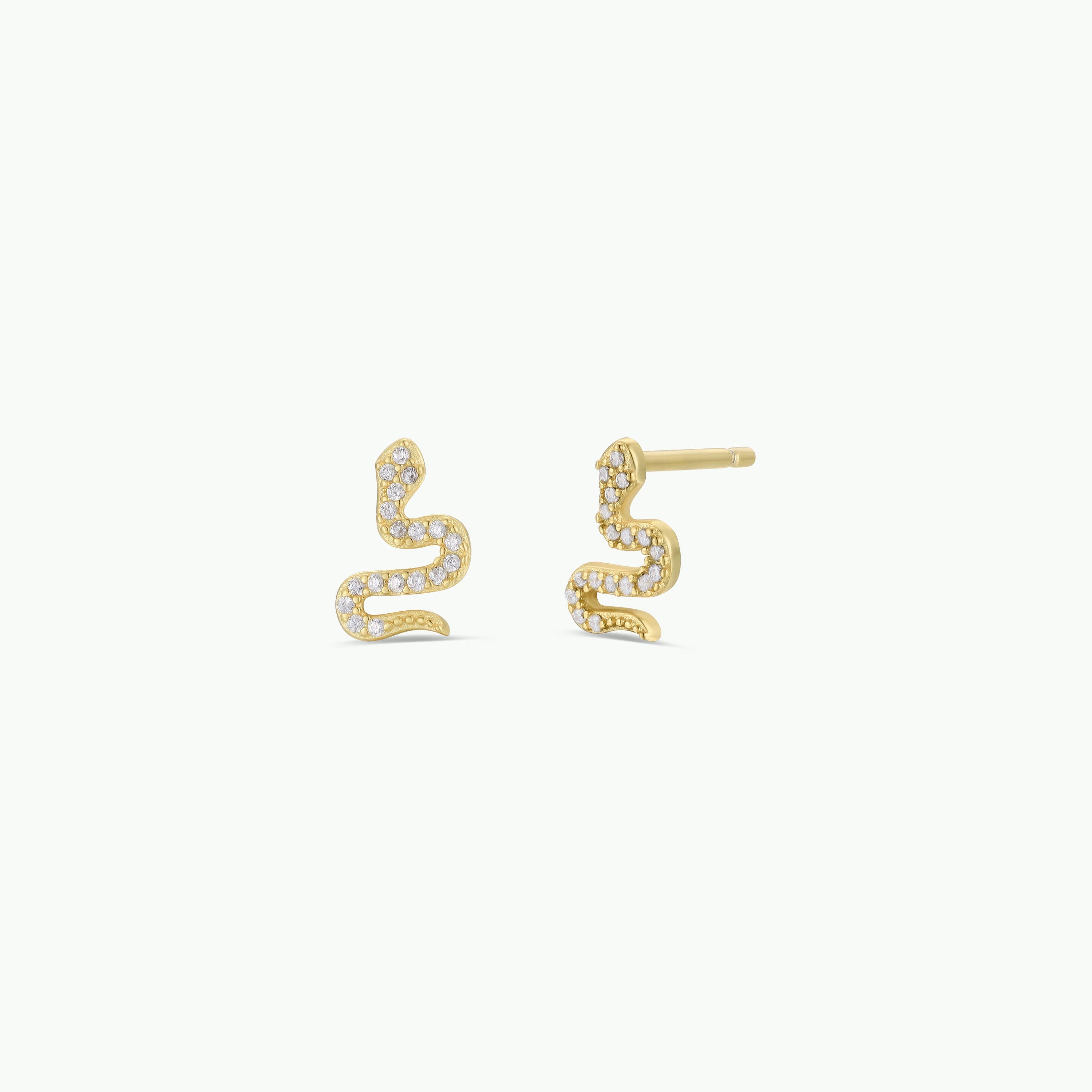 The Pavé Snake earrings are gold plated and serpent-shaped, each adorned with sparkling CZ stones along the body, shown against a plain white background.