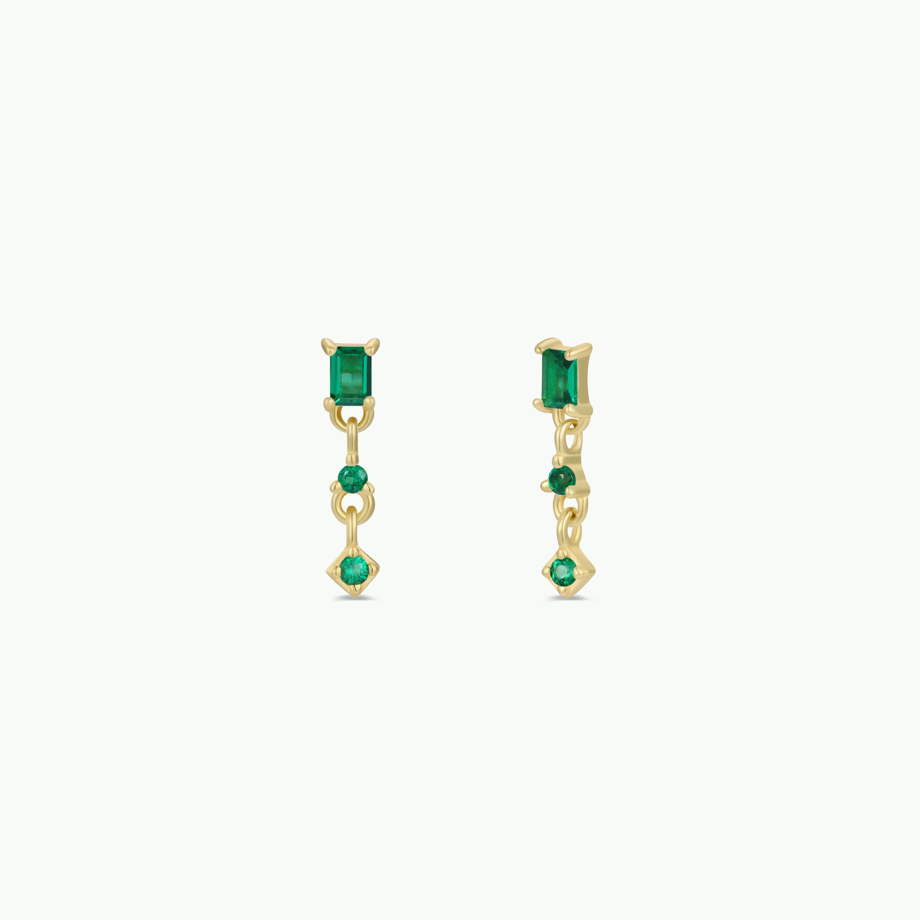 The Mini Baguette Drop Earrings - Emerald feature gold plating, an emerald baguette stud at the top, and two round CZ stones dangling below each earring.