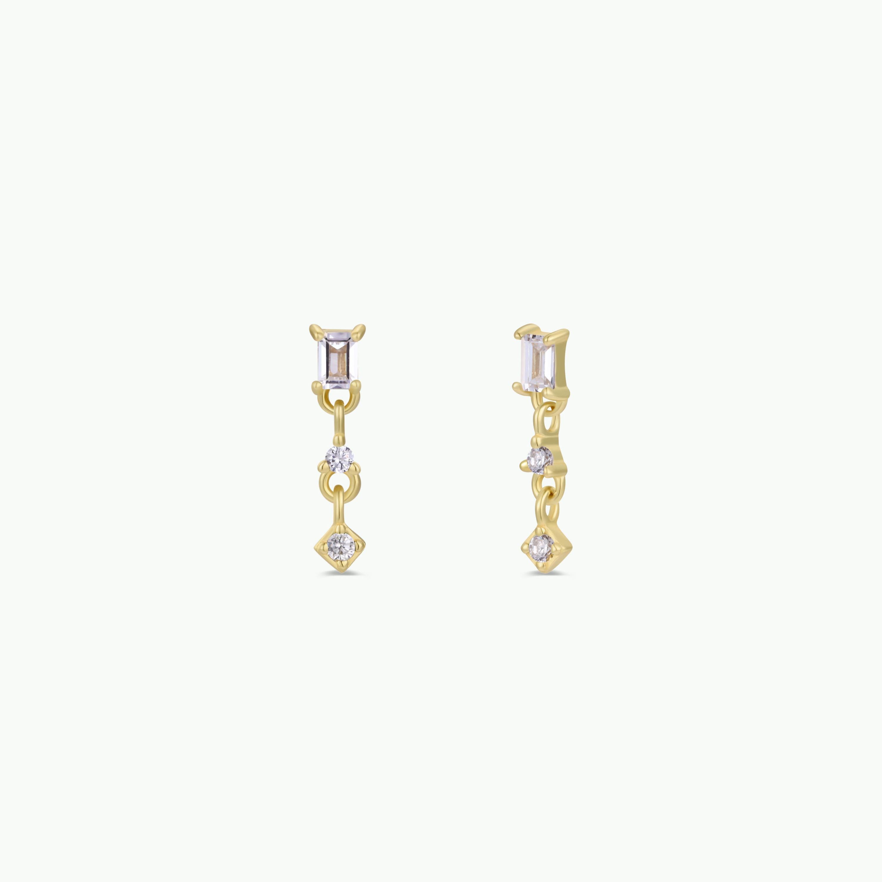 The Mini Baguette Drop - White features elegant gold drop earrings with rectangular and round CZ stones, delicate dangling design, 18K gold plating, and sterling silver posts, shown against a plain white background.