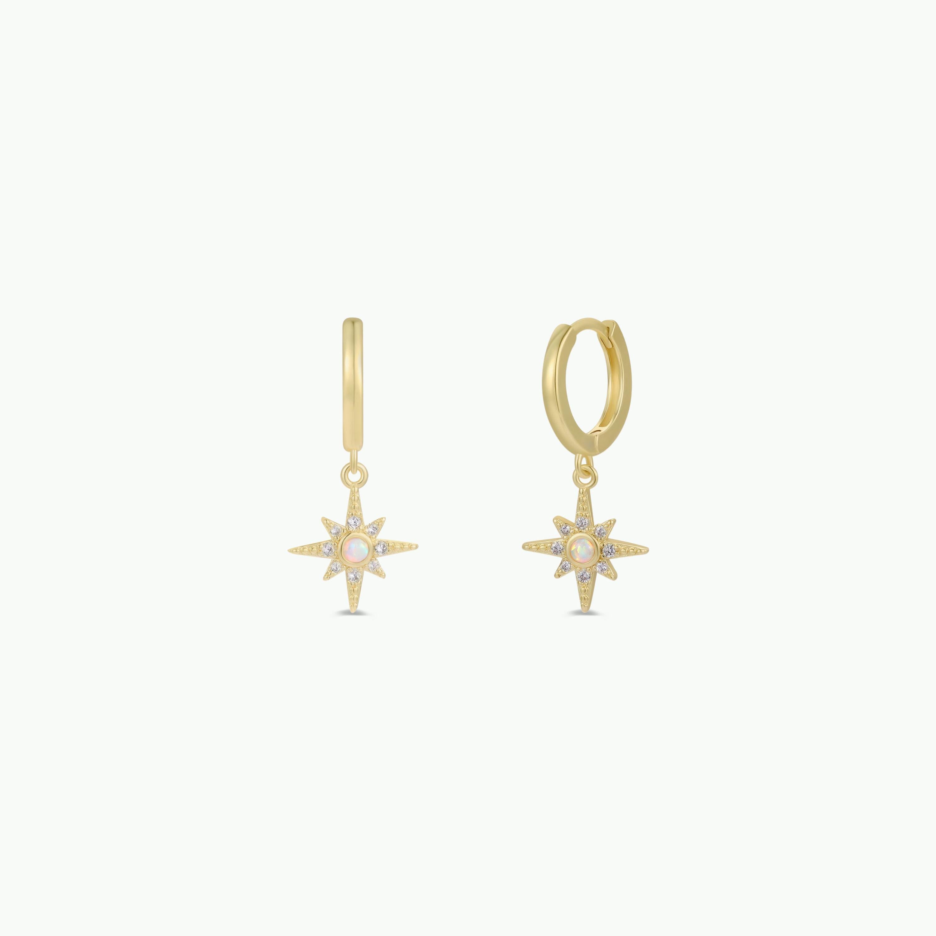 The Starburst Mini Hoop earrings feature gold hoops with starburst charm pendants, each adorned with a central white opal and smaller stones on the rays, shown against a plain white background.