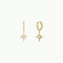 The Starburst Mini Hoop earrings feature gold hoops with starburst charm pendants, each adorned with a central white opal and smaller stones on the rays, shown against a plain white background.