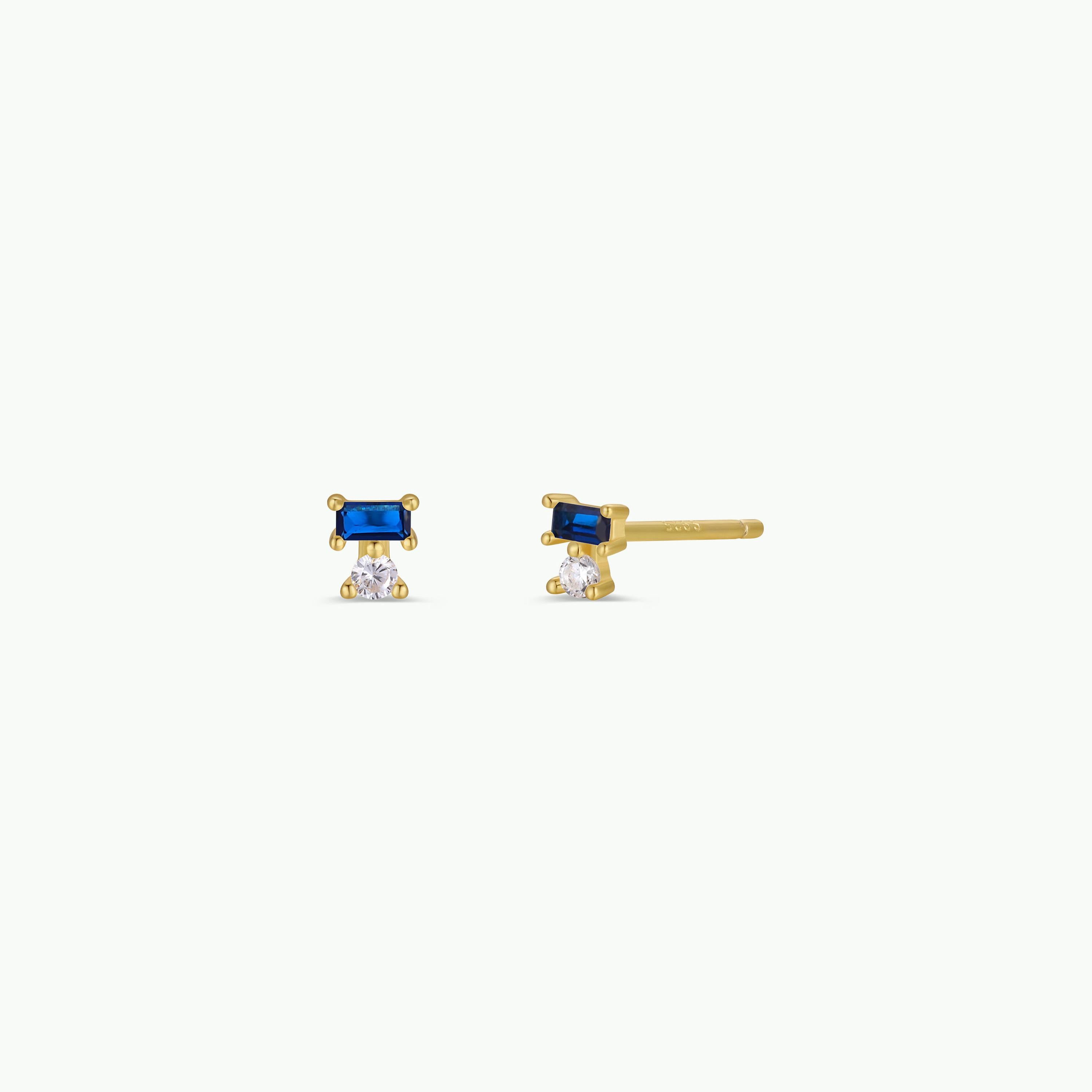 The Sapphire Double Stack is a pair of small gold stud earrings with a rectangular sapphire above a round CZ stone, finished in 18k gold plating and shown on a plain white background.