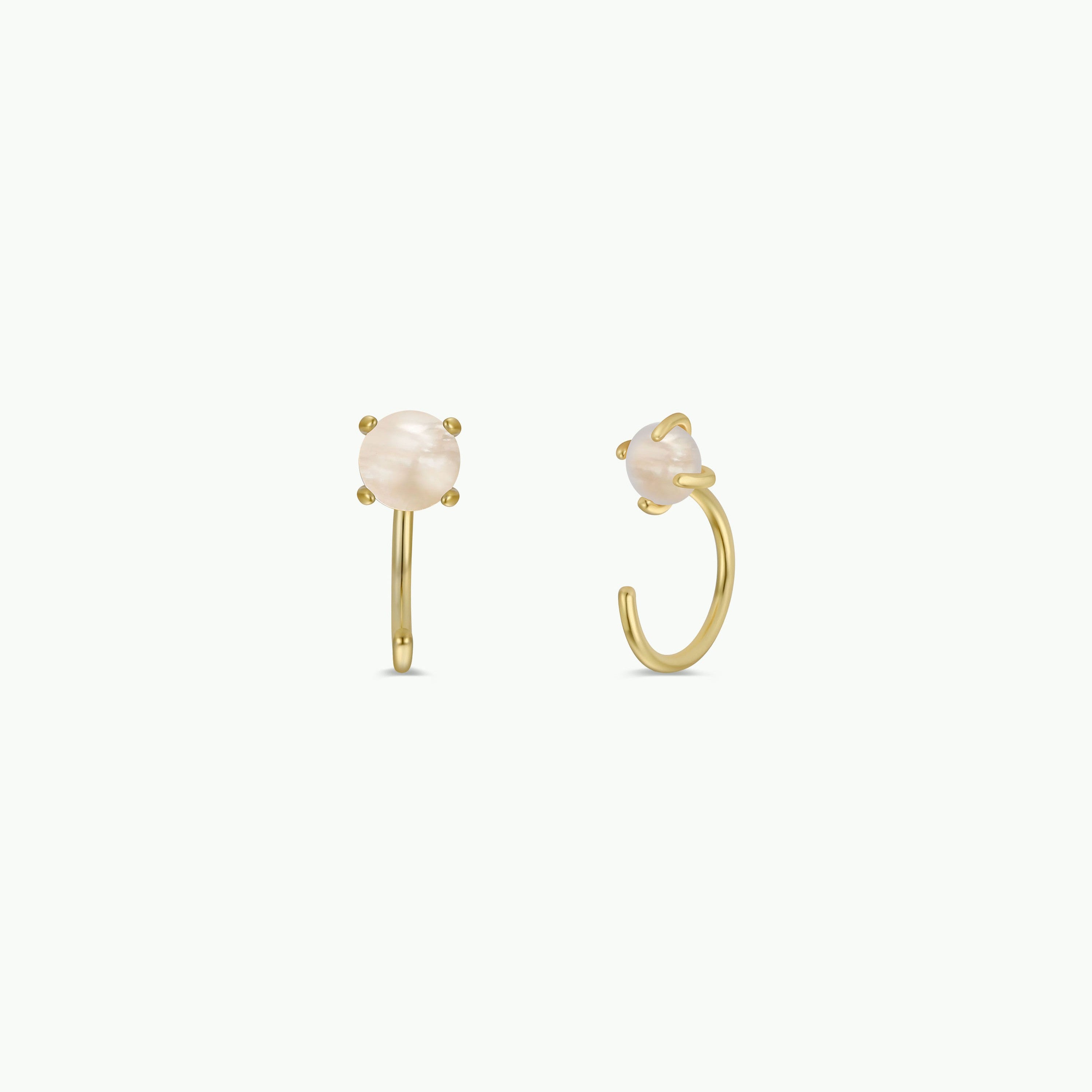The Mother of Pearl Huggie features gold huggie earrings with round, blush-colored stones in four-prong settings. These dainty, open-ended earrings have stones at the front and are shown against a plain white background.