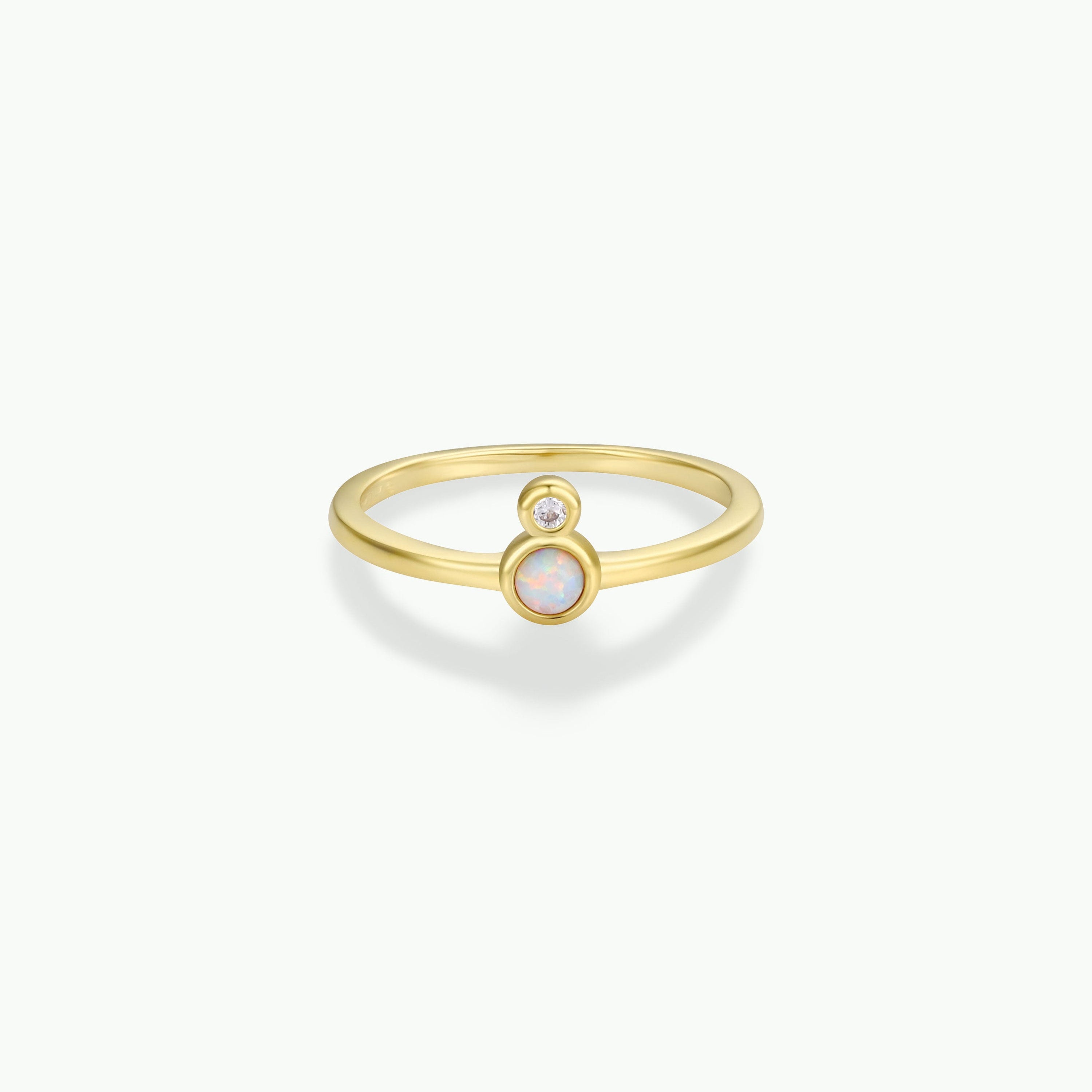 The Opal Infinity Ring is a delicate gold-plated piece featuring a round opal at the center and a small round diamond above it in bezel settings, displayed against a plain white background.