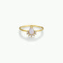 The Opal Burst Ring is an 18k gold-plated piece with a pear-shaped lab-grown Opal center, encircled by a halo of small round white diamonds, shown against a simple light background.