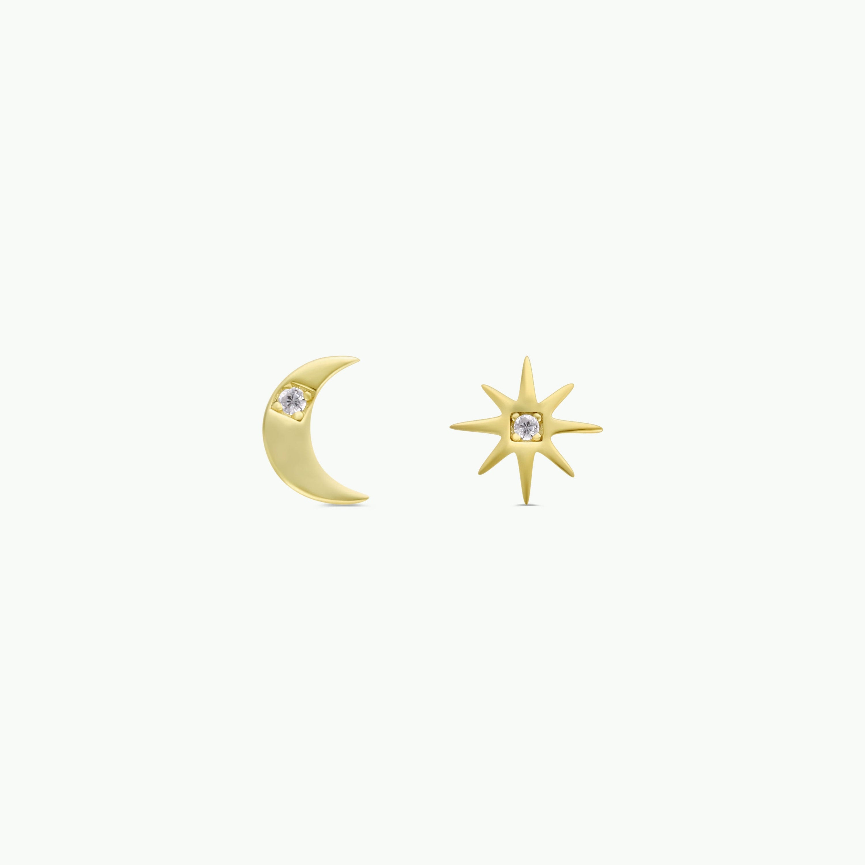 The Sun & Moon earrings are a mismatched pair of 18k gold-plated studs: one is a crescent moon with a small gemstone, and the other is an eight-pointed star with a central gemstone, shown on a plain white background.