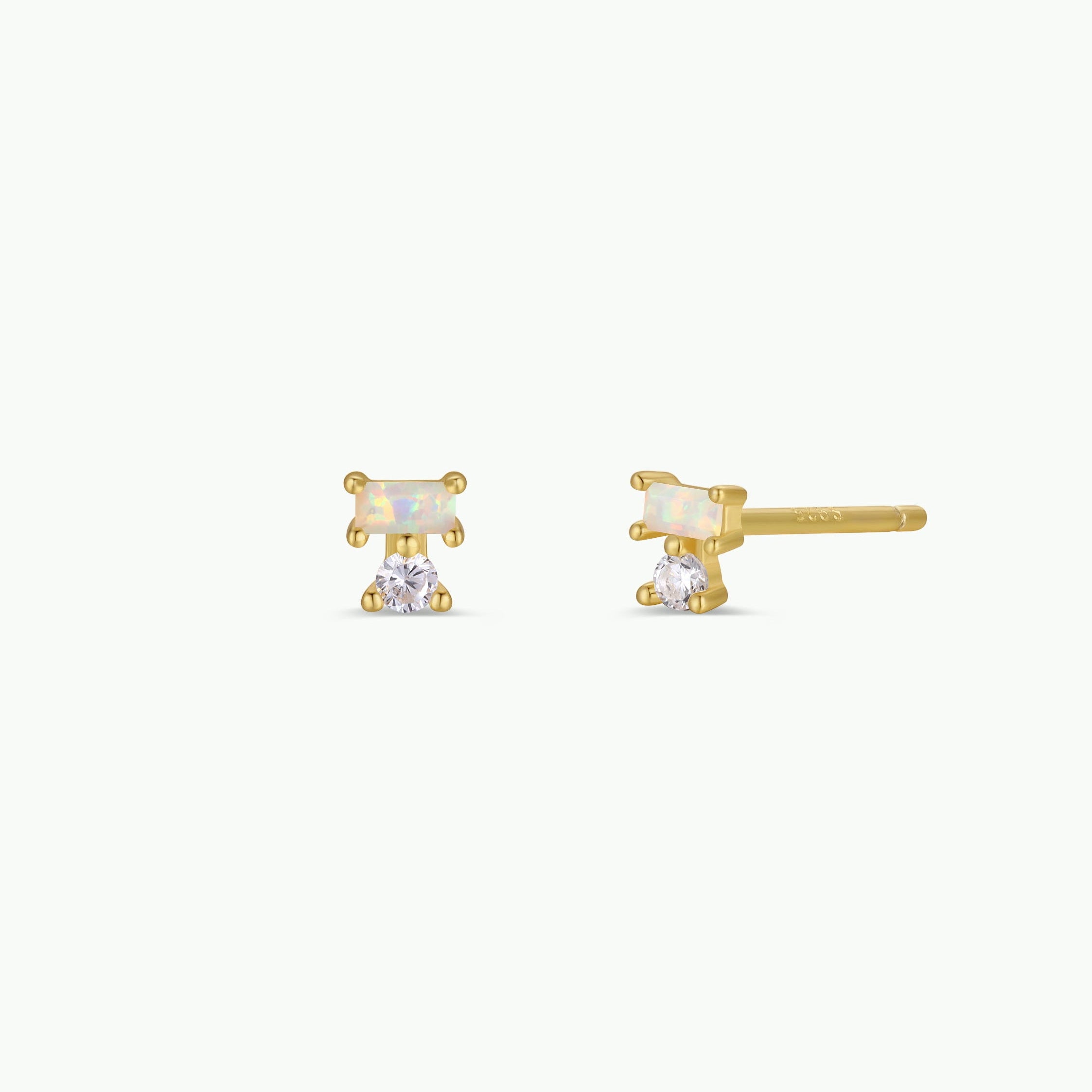 The JaxKelly Double Stud Stack - White Opal earrings feature a rectangular white opal at the top and a round white gemstone below, all set in luxurious 18K gold plating. Designed to be hypoallergenic, these elegant earrings offer comfort for sensitive ears and are beautifully presented against a white background.
