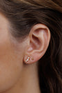 Close-up of a woman's ear wearing Crescent Gold Earrings - Pearl: a gold plated stud with three Mother of Pearls in a row, plus a delicate gold stud. Sterling silver posts offer comfort. Her brown hair is tucked back, and her skin appears smooth and natural.