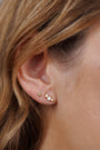 Close-up of a woman's ear with two piercings: one wears the Tiny Star mini stud earring on sterling silver, the other shows an 18k gold plated earring with three white stones. Brown hair frames her ear.