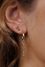 Close-up of a person’s ear wearing gold plated Coffee Baguette stud earring with sterling silver post in the upper lobe, and a gold hoop with four dangling round gemstones below. Strands of light brown hair are visible.