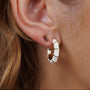 Close-up of a person’s ear wearing two earrings: a small rectangular stud and the Vintage Hoop Earrings - Cream Enamel. The larger earring features cream enamel with gold accents. The person's light brown hair is partially visible.