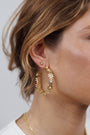 Close-up of a woman's ear wearing a large floral gold hoop earring, paired with the Petite Daisy Stud in an elegant ear stack. Part of her face and brown hair are visible.