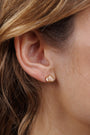 Close-up of a woman's ear with wavy brown hair, wearing JaxKelly's Champagne Baguette Crown Earrings—18K gold plated, tarnish-free studs featuring three clear rectangular gemstones in a fan shape.
