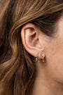 Close-up of a woman's ear framed by brown hair, wearing the Small Channel Gold Hoop—a thicker, ridged 18K gold plated earring with a sterling silver post—paired with a thinner gold hoop featuring a small charm.