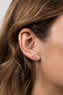 Close-up of a woman's ear wearing JaxKelly's Studded Threader - Mother of Pearl, along with a star-shaped stud and a small round stud. Her brown hair is tucked behind her ear as the threader earring dangles gracefully.
