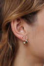Close-up of a woman's ear with three gold earrings: a triangle stud, an abstract stud, and the Small Ripple Gold Hoop—featuring 18K gold plating and sterling silver posts. Her light brown hair is tucked behind her ear.