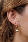 Close-up of a woman's ear wearing the Seashell Hoop Earring: a gold-plated hoop with a seashell charm and sterling silver post, paired with a triangle stud. Her brown hair elegantly frames the look.
