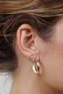 Close-up of a woman's ear wearing the White Opal Sun Stud, featuring a lab-grown white opal center with 18k gold plating in the upper lobe, and a larger gold hoop in the lower lobe. Hair is pulled back to showcase the earrings.