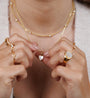 A person holds the Mother of Pearl Heart Pendant Necklace, wearing several gold rings and a layered necklace with small gems. The jewelry is the focus, while their face remains out of view.