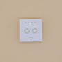 A pair of Round - White Opal Gemstone - Gold Earrings sits on a white Jax Kelly “Opal joy” card against a beige background.