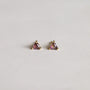 A pair of Mystery Earrings featuring small gold triangles with purple gemstones at the center, displayed on a smooth, light surface.