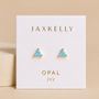 A pair of JaxKelly Fire Opal Mini Energy Gems - Joy studs with gold trim and lab-grown fire opal sit on a white card with gold "JAXKELLY OPAL joy" text, displayed against a beige background.