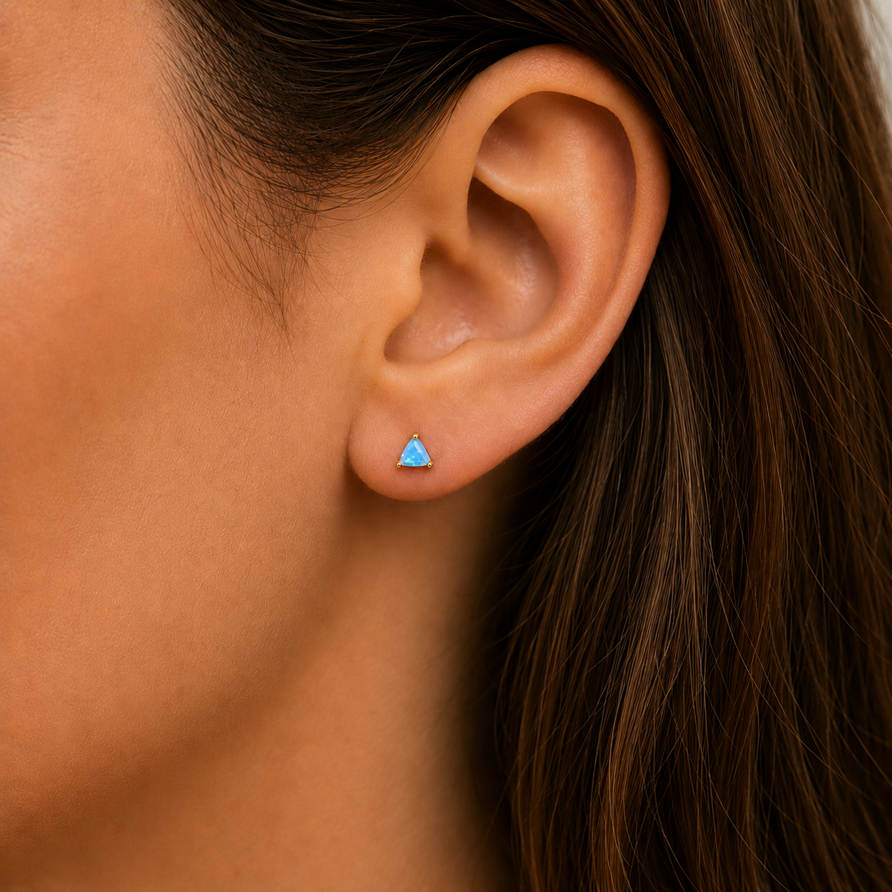 Close-up of a woman's ear with straight brown hair, wearing JaxKelly's Fire Opal Mini Energy Gems - Joy, featuring lab-grown fire opal and 18k gold plating.