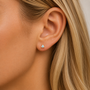 Close-up of a woman's ear with light skin and blonde hair, wearing JaxKelly's White Opal Mini Energy Gems - Joy stud earring set in 18k gold plating.