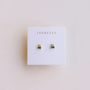 A pair of Double Stud Stack - Emerald CZ earrings by JaxKelly, gold plated with emerald baguette and clear round stones, displayed on a white JaxKelly card. These hypoallergenic studs provide stylish comfort for sensitive ears.