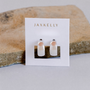 A pair of Silver Wide Hoop sterling silver earrings from JaxKelly, shown on a white card with gold lettering, propped against a textured stone background.