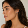 A woman with long brown hair and clear skin looks to the side, wearing JaxKelly’s Offset Trio - Fire Opal earrings and a white top, set against a neutral background.