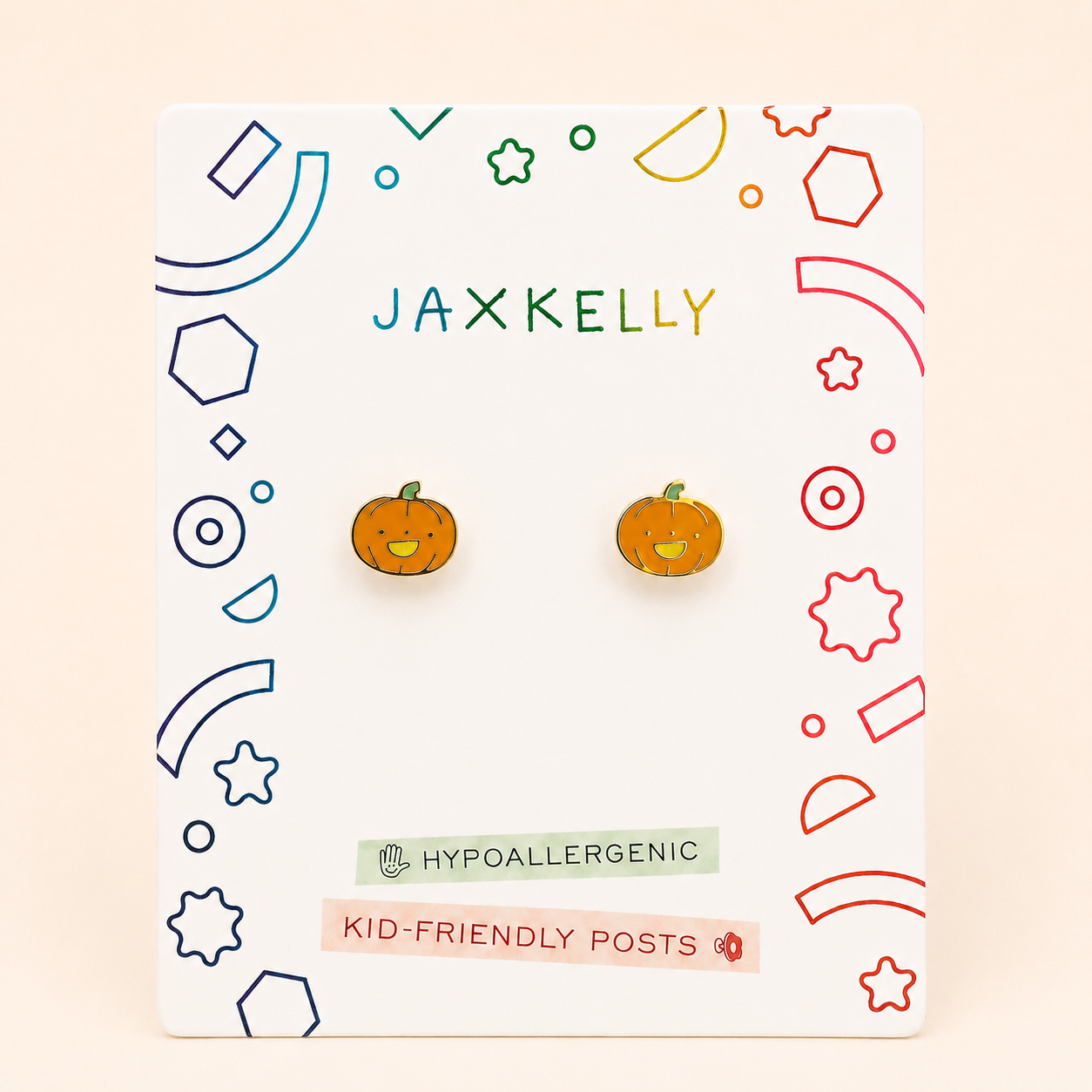A pair of JaxKelly Pumpkin Enamel Flat Back Kids Earrings displayed on a card with colorful geometric designs. Labels highlight kid-friendly posts and hypoallergenic earrings, making them perfect for sensitive ears.