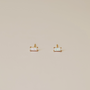 The White Opal Baguette stud earrings, featuring lab-grown white opals with an iridescent sheen set in 18k gold plating, are shown side by side on a smooth light beige surface.