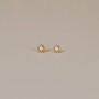 The White Opal Sun Stud features lab-grown white opal centers in a sun-inspired design, crafted with 18k gold plating and sterling silver posts, shown on a neutral light beige surface.