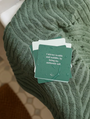 The Abundance Shower Affirmations™ is a stack of green waterproof cards with abundance quotes and water droplets, resting on a textured green towel. The top card reads, “I attract wealth and stability by being my authentic self.”.