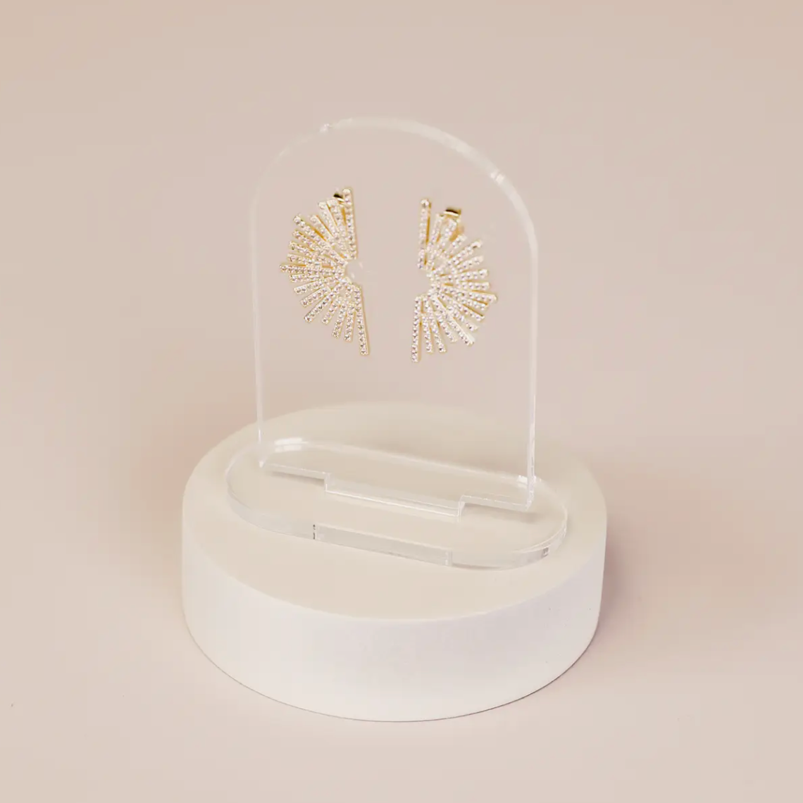 Gold, fan-shaped earrings with sparkling stones are displayed on the Clear Earring Display Arch Solid, featuring a clear acrylic stand with a round white base, all set against a light beige backdrop for an elegant retail look.