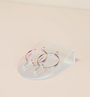 The Iridescent Earring Display Bent Large showcases a pair of gold hoop earrings with clear quartz pendants, set on a transparent iridescent stand against a light, neutral background.