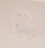 A pair of gold hoop earrings with light blue vertical stone pendants is displayed on the Clear Earring Display Hollow Arch, set against a pale pink background for a chic retail look.