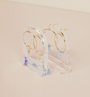 Two pairs of gold hoop earrings with gemstone dangles are showcased on Clear Earring Display Hollow Arch stands, highlighting a refined retail look against a soft beige background.