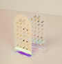 The Clear Earring Display Stud Arch showcases multiple pairs of small, colorful earrings—flowers, animals, and geometric shapes—on a light beige surface, making it ideal for stylish JaxKelly or any retail display setting.
