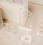 A retail display features gold jewelry, including colorful gemstone earrings on the Clear Earring Display Stud Arch, gold hoop earrings, and a triangular-design gold ring, all arranged on a light-colored surface inspired by JaxKelly.