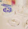 The Iridescent Ring Display Circle showcases a gold ring with a triangular black stone, surrounded by minimal gold jewelry on stands atop a white surface—ideal for chic retail merchandising displays.