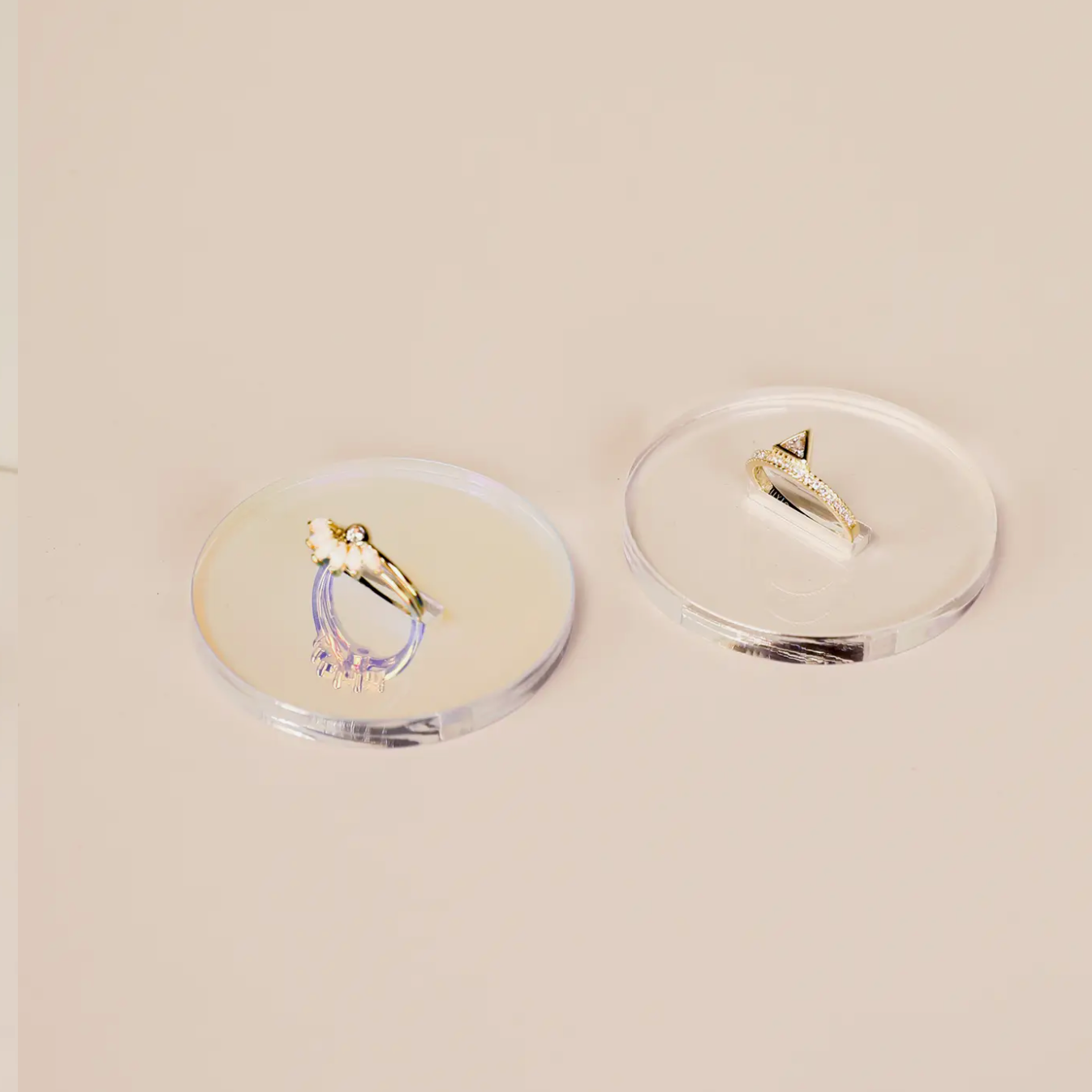 Two gold rings and a gold earring rest on separate Iridescent Ring Display Circles against a light beige background.