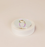 The Iridescent Ring Display Circle elegantly showcases a gold ring with a white flower design and central gemstone against a plain beige background, highlighting the refined style of JaxKelly displays.